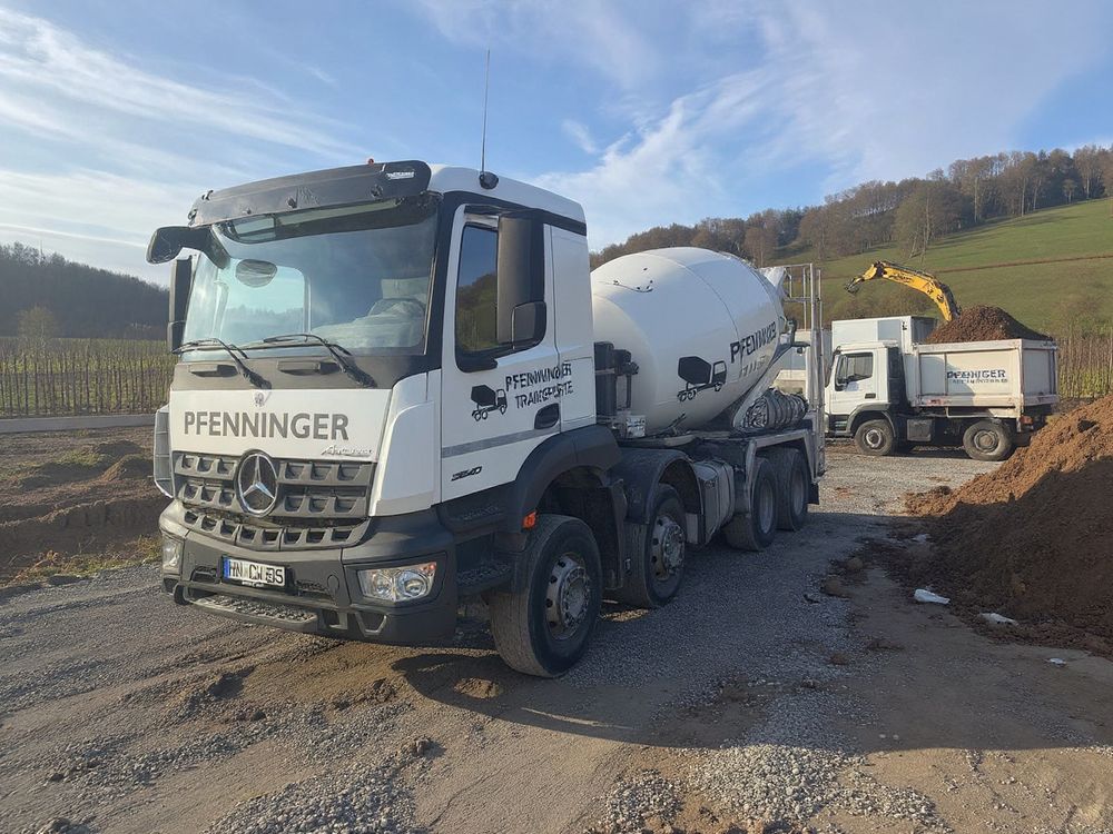 Pfenninger-Fahrmischer an einer Baugrube, im Hintergrund belädt ein Bagger einen Kipper mit Erdaushub, Weinberge in der Ferne