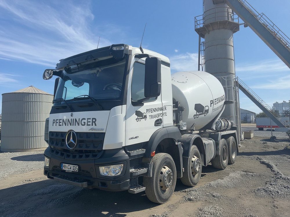 Pfenninger-Fahrmischer auf dem Gelände eines Transportbetonwerks vor Silos und Förderanlage unter blauem Himmel