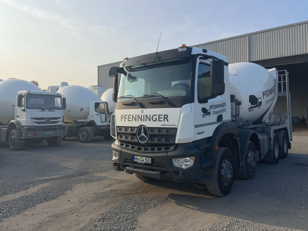 Weißer Pfenninger-Fahrmischer (Mercedes-Benz Arocs, vier Achsen) auf einem Betriebshof mit weiteren Fahrmischern vor einer Fahrzeughalle